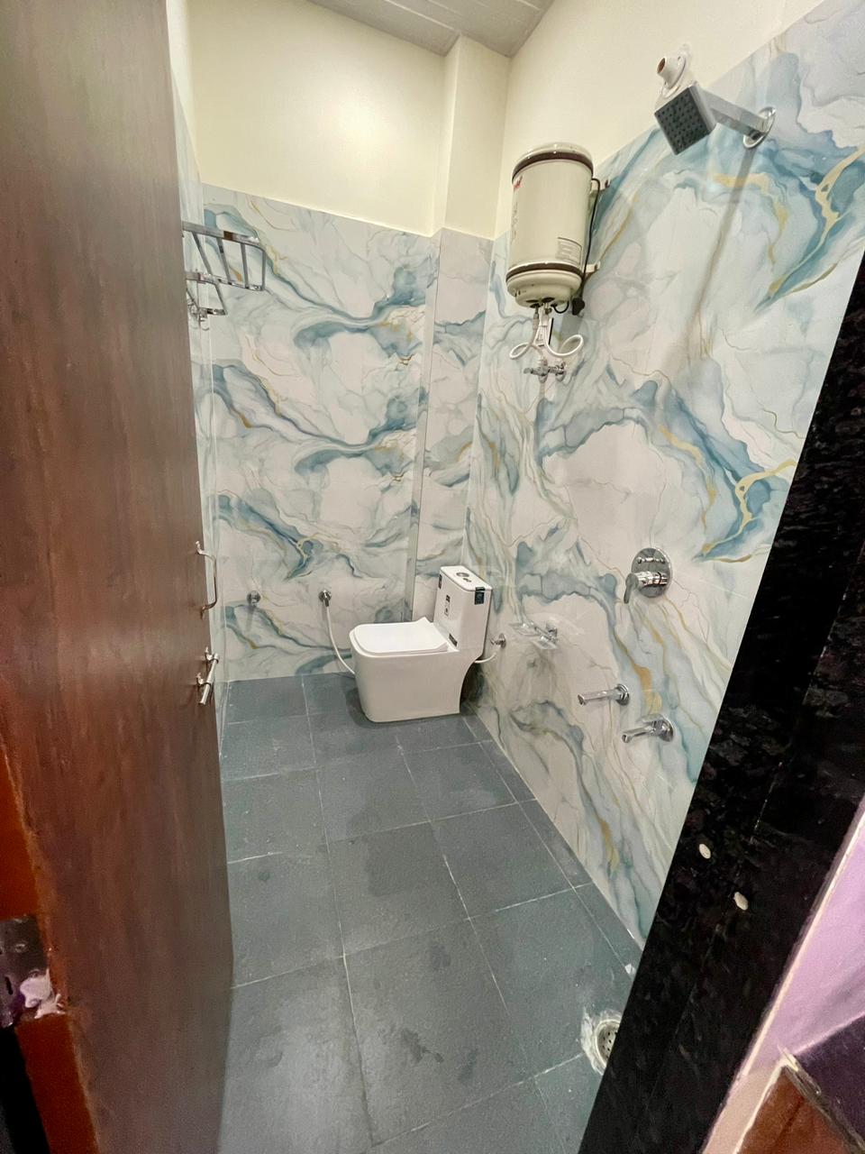 Modern bathroom featuring full-height ocean marble glazed vitrified tiles, wall-hung Western commode, shower mixer, and geyser installation