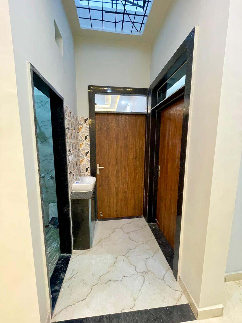 Inner hallway with polished wooden doors in black granite frames, handwash corner with 3D prism tiles, and overhead ventilation cutout