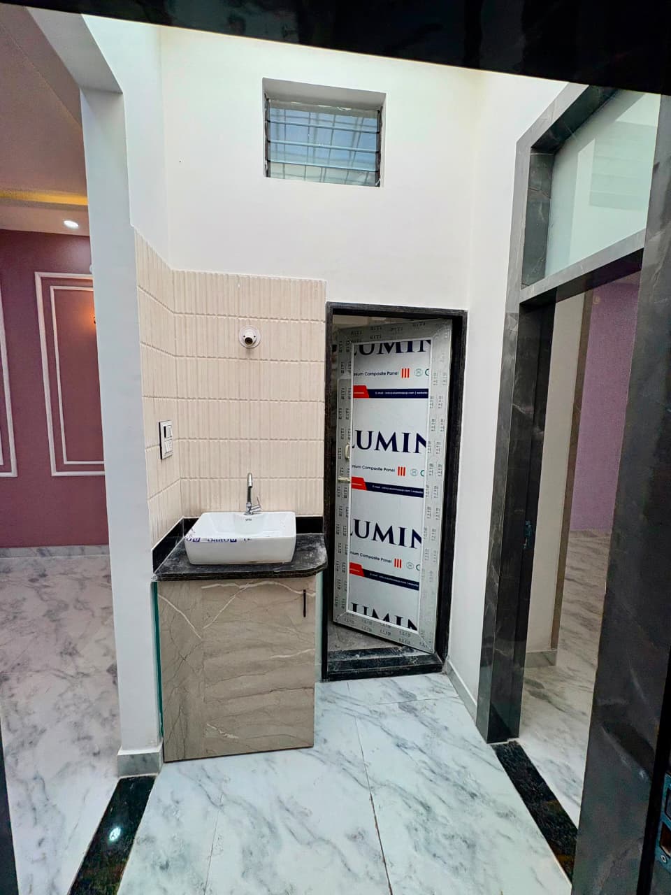 Handwash vanity station with ceramic countertop basin, storage cabinet, textured fluted wall tiles, and marble flooring