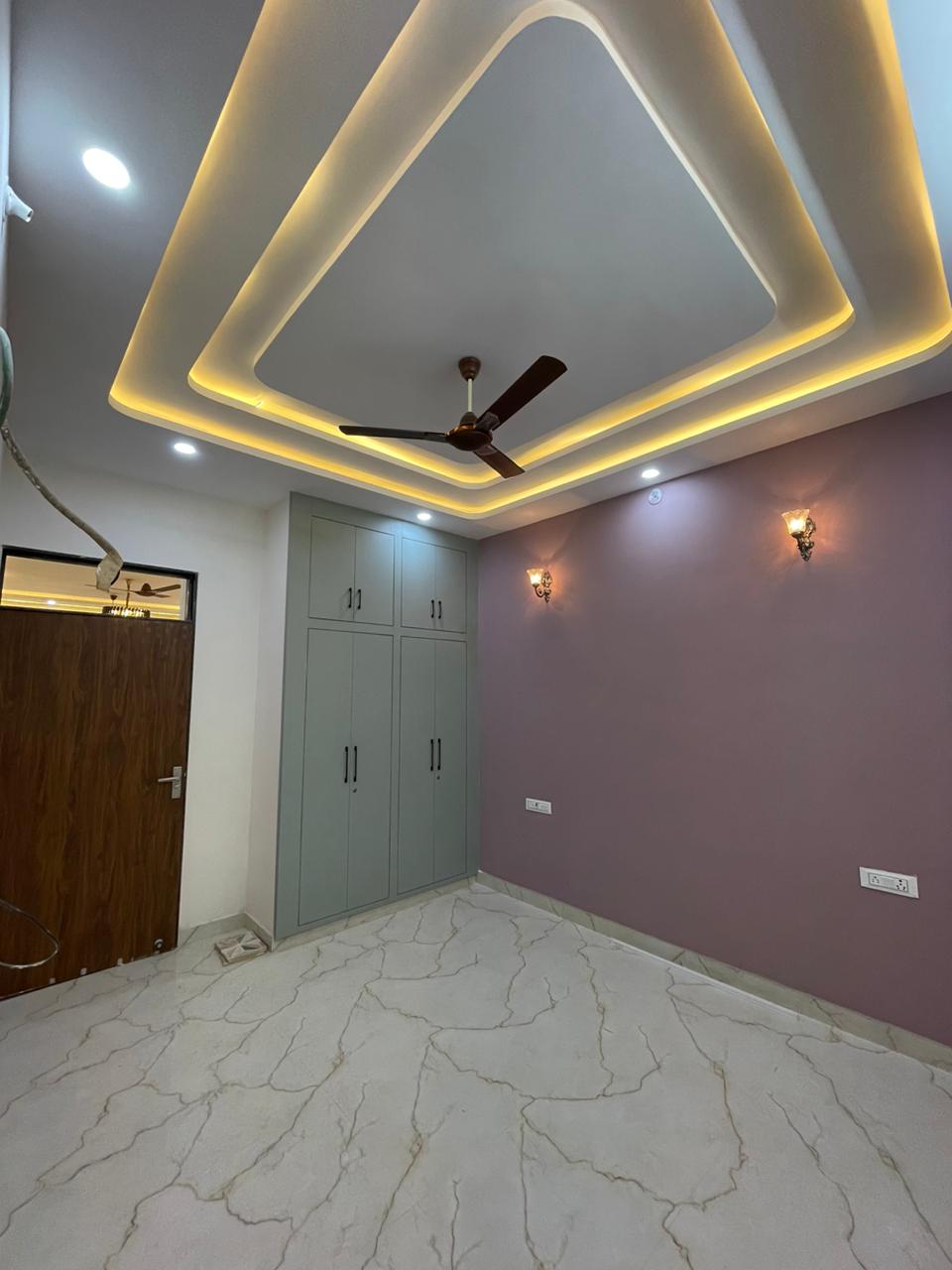 Calming bedroom interior with muted grey floor-to-ceiling wardrobes, mauve feature wall with wall lamps, and concentric false ceiling illumination