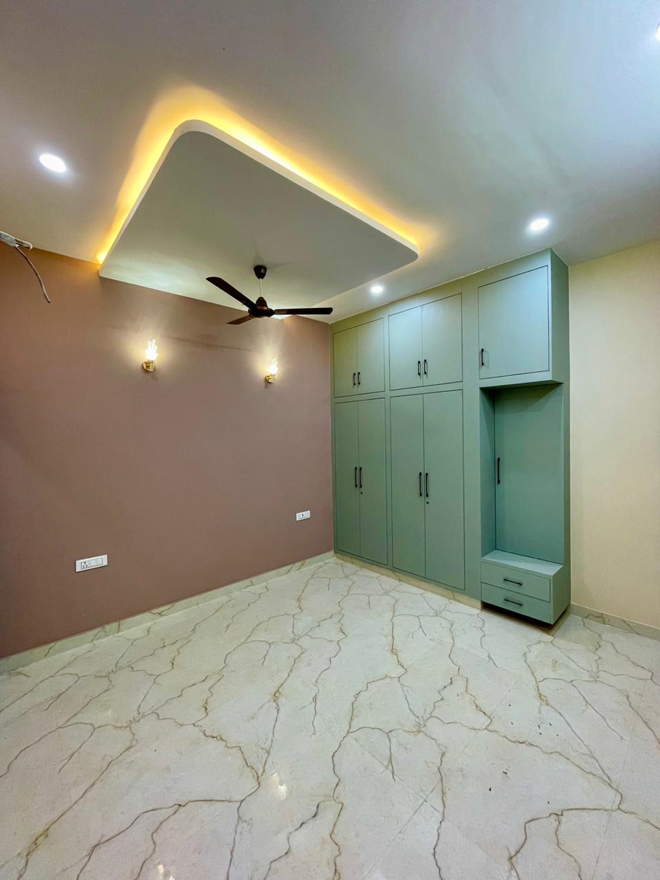 Serene bedroom with bespoke sage green wardrobe and dressing niche, mauve accent wall, sconce lighting, and cove ceiling