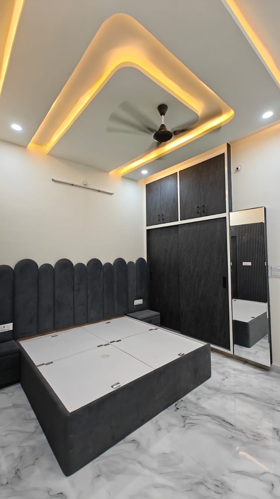 Master bedroom with dark wood sliding wardrobes, full-length dressing mirror, velvet upholstered bed, and warm perimeter ceiling lighting