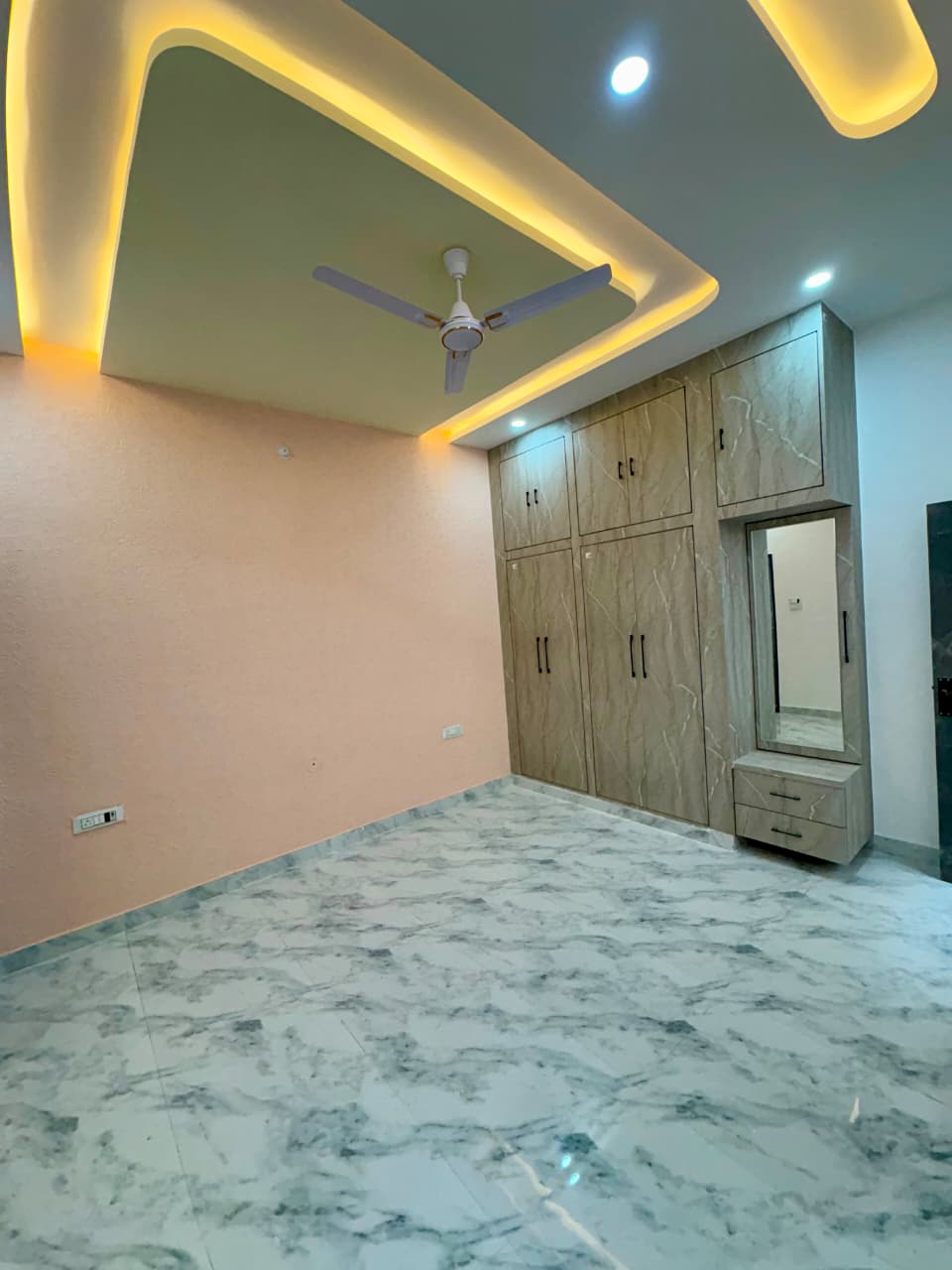 Modern bedroom with warm false ceiling cove, marble flooring, and floor-to-ceiling built-in wooden wardrobes with dressing mirror