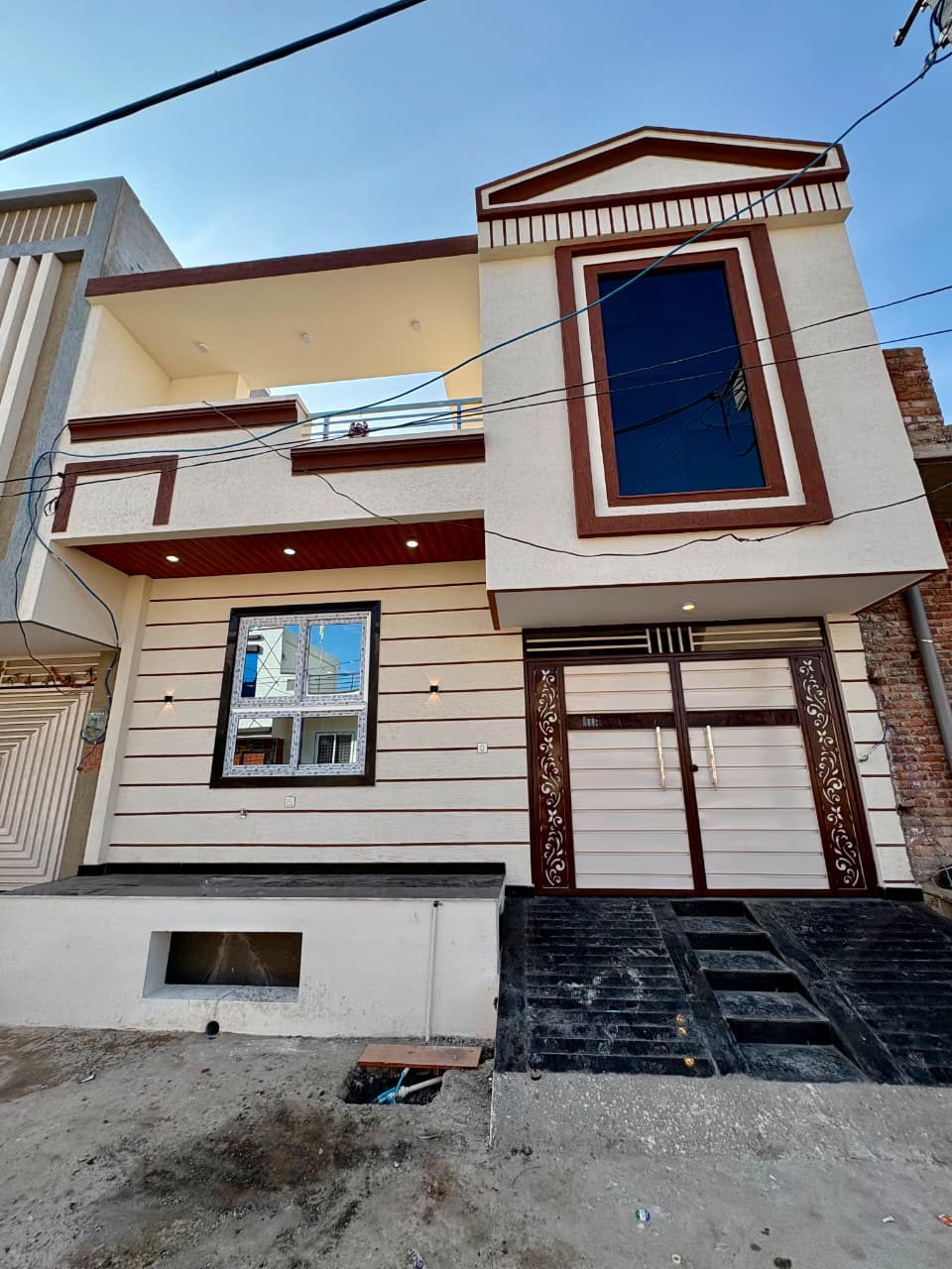 Completed modern 2-story residential bungalow elevation with balcony glass railing, wood finish, and designer entrance gate by Dream Construction Kota