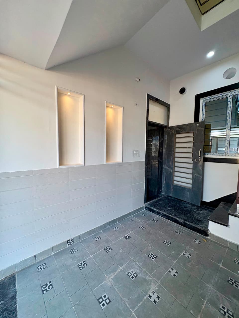 Covered entrance porch and foyer with recessed illuminated wall niches, patterned vitrified tiles, and heavy-duty main security door
