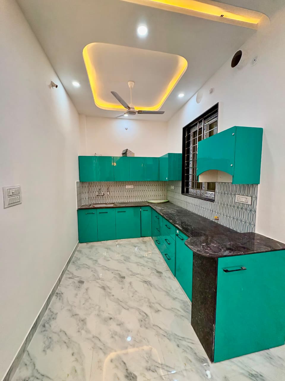 Vibrant teal and cyan modular L-shaped kitchen with black granite countertop and dual cove ceiling lighting
