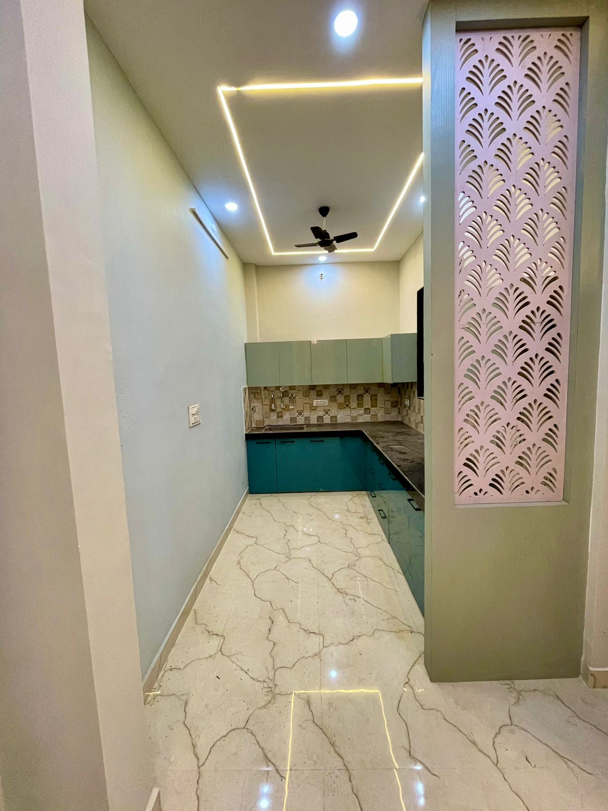 Modular kitchen with contemporary two-tone teal and mint cabinetry, black granite slab, and decorative CNC floral jali screen partition