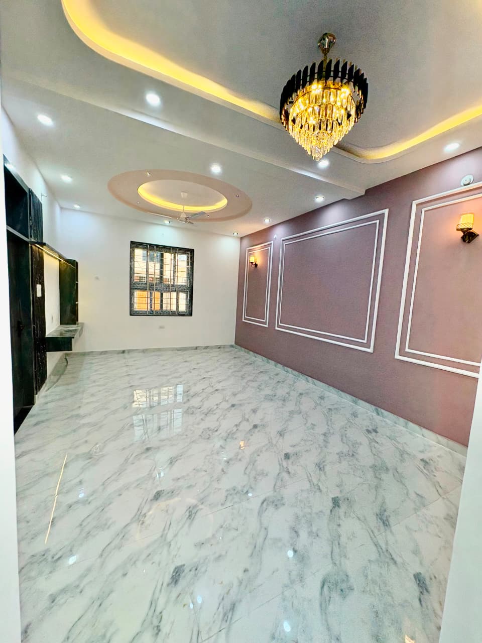Expansive family living hall with French wall paneling, circular chandelier ceiling feature, and high-gloss vitrified marble flooring