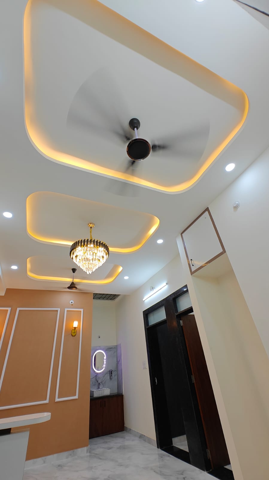 Central corridor and living hall perspective showing layered false ceiling levels, hanging chandelier, and backlit LED vanity mirror