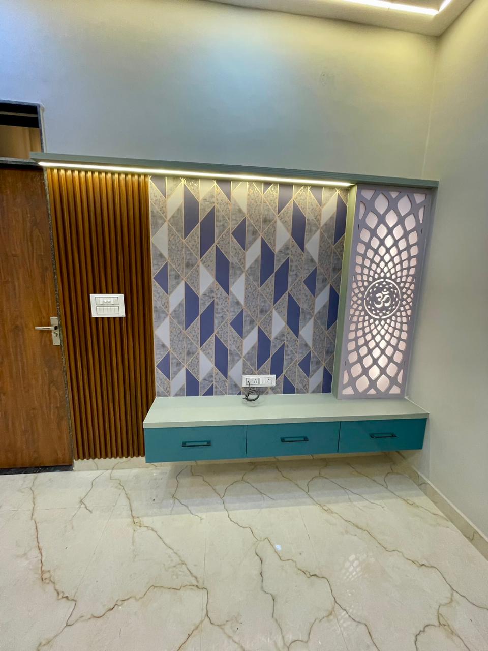 Designer TV media console with turquoise floating drawers, vertical timber louvers, geometric stone wallpaper, and illuminated laser-cut Om mandir jali