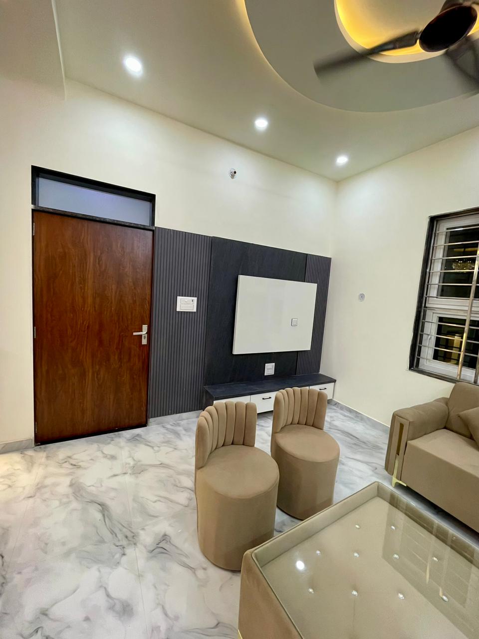 Reception room with dark fluted TV backdrop wall, wall-mounted display console, plush cylindrical armchairs, and rich polished teak door