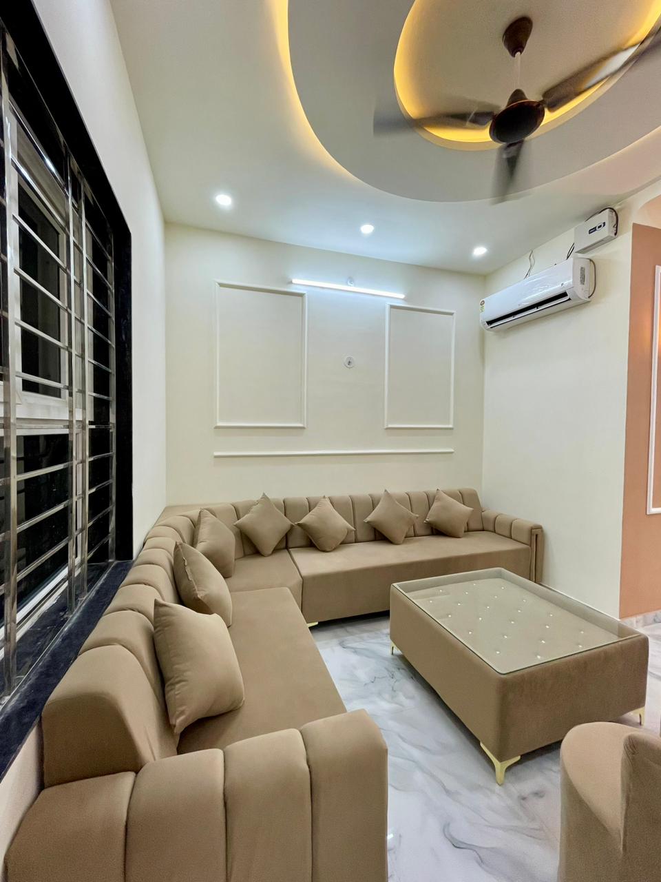 Cozy family lounge with custom beige sectional sofa, matching upholstered coffee table, classical wall moulding panels, and circular cove lighting